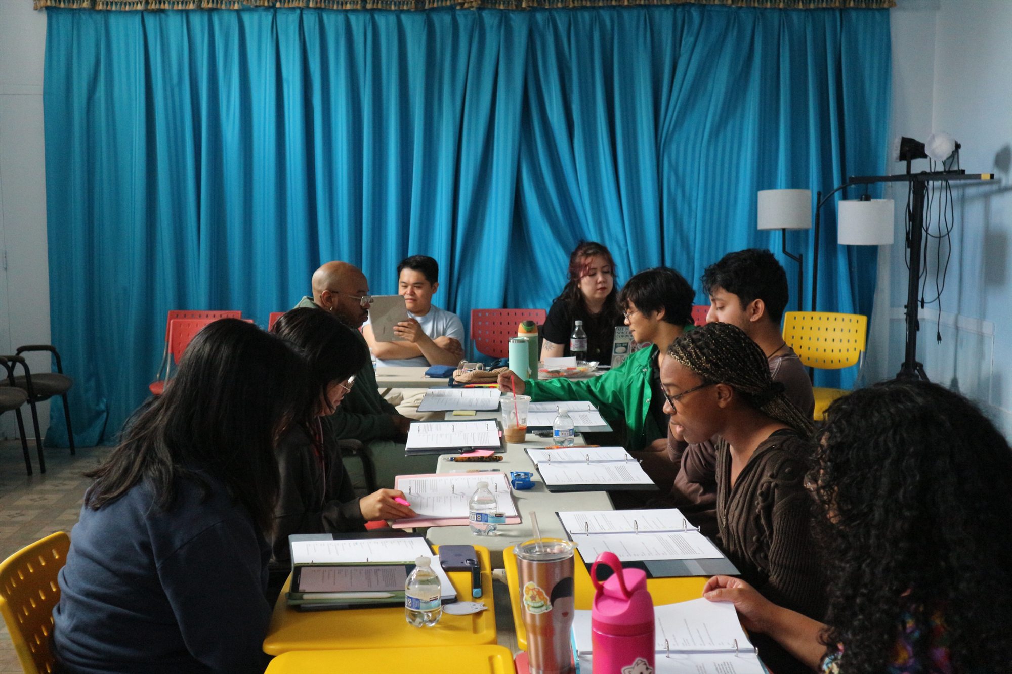 CIRCA Pintig creative staff and cast gather around tables with scripts and binders during a rehearsal.